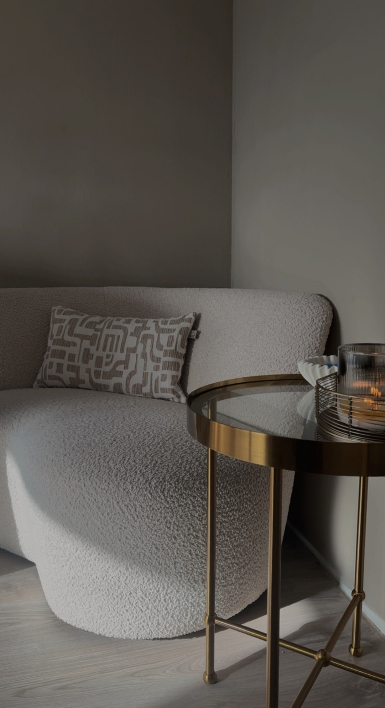 Een hoek van de salon met een bouclé stoel en een glazen bijzettafel
